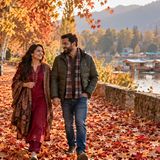 Videographer filming a couple with a phone gimbal on a path of autumn chinar leaves