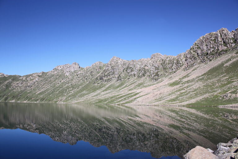 Tarsar Lake reflecting a rocky ridge on a clear day