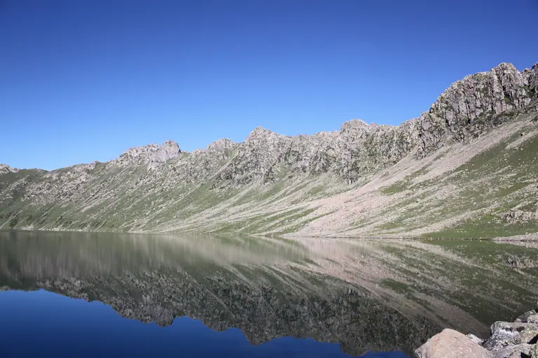 Tarsar Lake reflecting a rocky ridge on a clear day